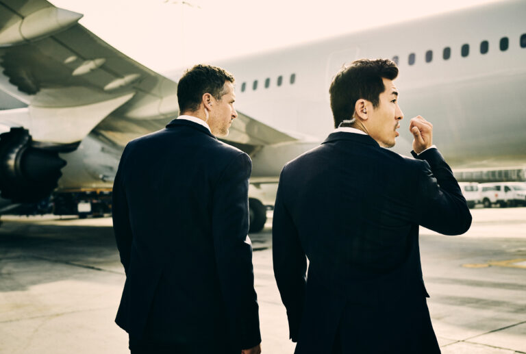 Two PS team members standing on tarmac with plane in background.