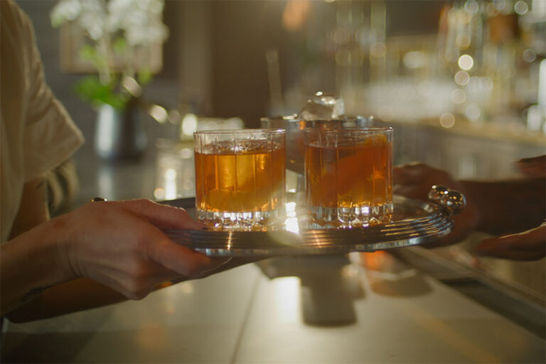 Bartender passing drinks on a tray to PS Salon server.